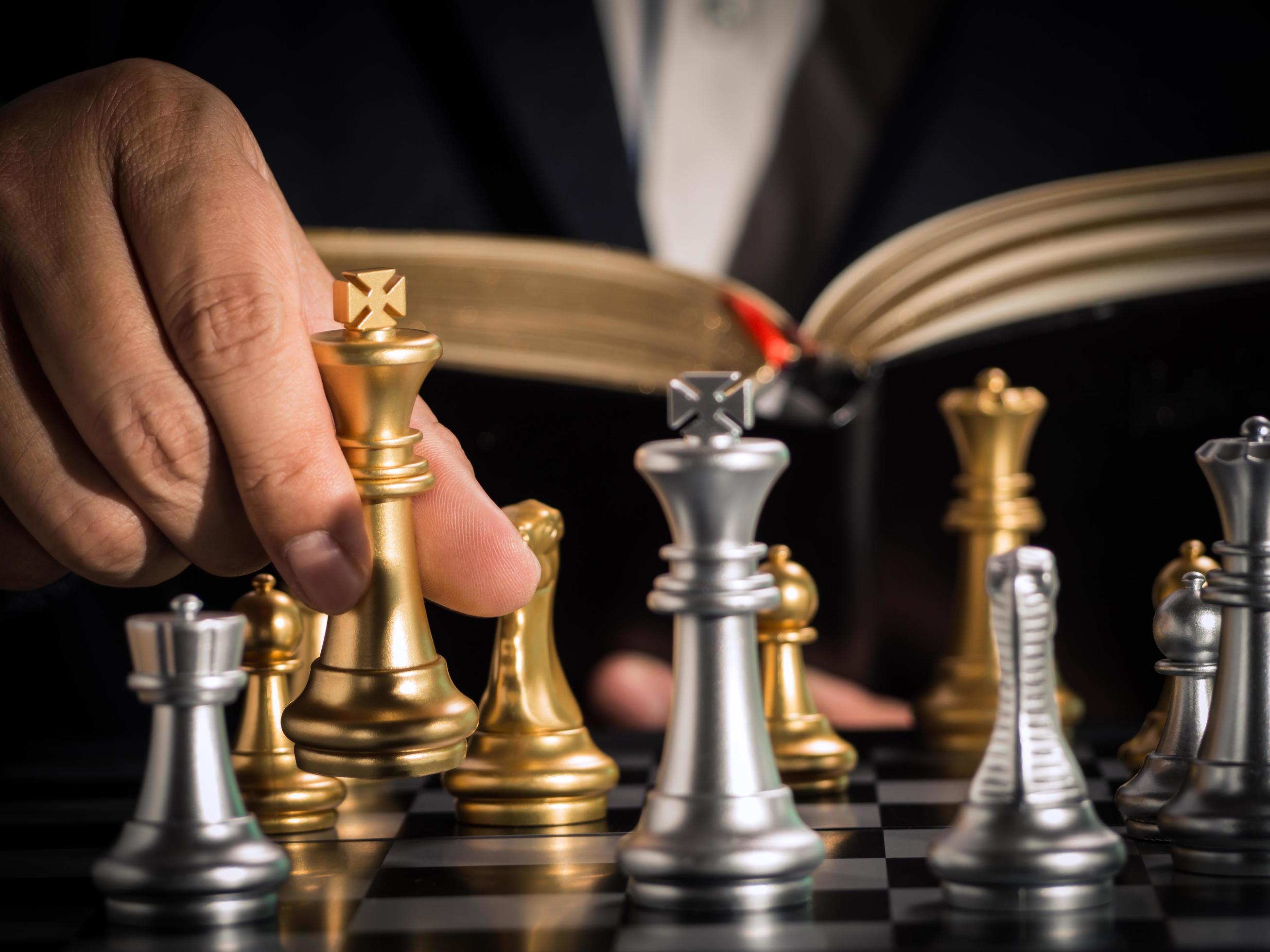 mão do empresário movendo o xadrez rei dourado para lutar contra o xadrez  rei prata com a diretriz do livro de abertura jogar com sucesso na  competição. estratégia de gestão ou liderança